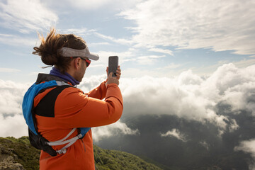 A man in an orange jacket is taking a picture of the mountains