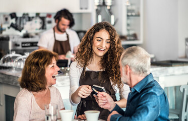 Beautiful female barista working in coffee shop, serving customers, elderly couple. University student working part-time in cafe.