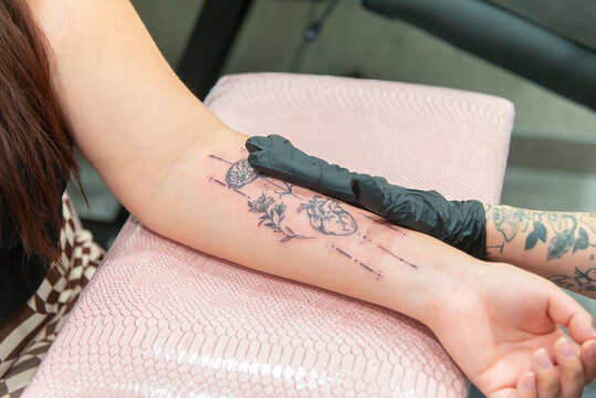 Anonymous artist creating a floral forearm tattoo