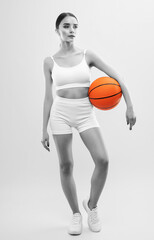 A beautiful slender girl athlete in shorts and in white top plays basketball.