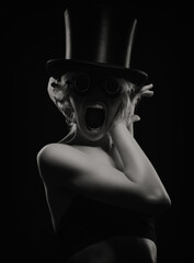 Portrait of a girl in black glasses, a black hat on a black background. She holds a knife in her hand. one of the symbols of halloween