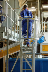 Worker in blue uniform and hard hat standing on a platform in an industrial recycling facility,...