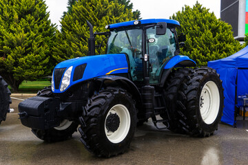 The new blue agricultural tractors of various models stand in a row at the exhibition site in...