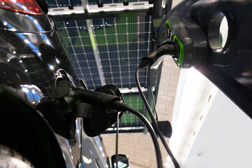 Electric car is charged from a charging station that takes energy from solar panels. Close up..