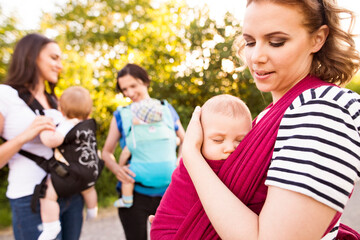 Mothers carrying babies in carriers, slings or wraps. Babywearing.