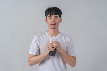 Handsome young man drinks soda and holding plastic cup and soda bottle.