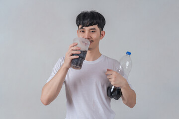 Handsome young man drinks soda and holding plastic cup and soda bottle.