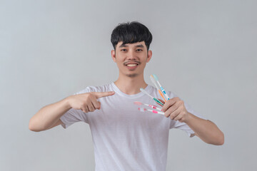 Handsome young man holding several colorful toothbrushes.