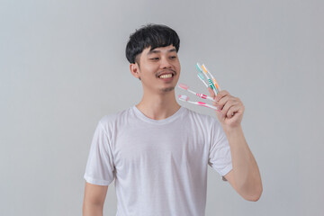 Handsome young man holding several colorful toothbrushes.