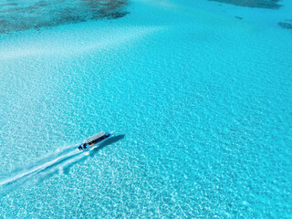 Aerial view of floating boat in clear azure water in summer. Zanzibar island. Top drone view of...