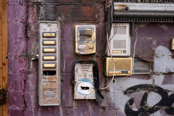 Grungy wall with weathered intercoms and vandalized mailbox, showcasing urban decay and neglect in a city environment.