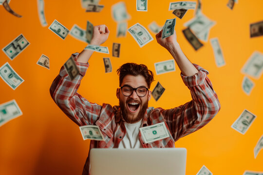 Happy man celebrating in front of a laptop because he winning a big prize, money floating, orange background