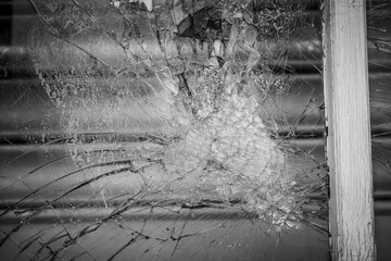 Close-up of a shattered glass window capturing the intricate web of cracks and central impact point...