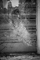 Close-up of shattered window pane with cracked glass, highlighting textures and decay in monochrome.