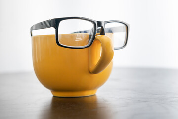 Front view on yellow cup with eyeglasses on it. Creative idea and coffee for business concept	