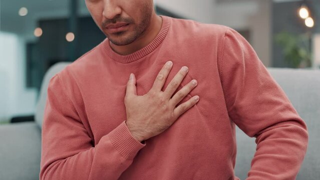 Man, hand and chest pain with injury, heart attack or ache on living room sofa at home. Closeup of male person in panic, cardiac arrest or stroke on couch from stress, anxiety or strain at house