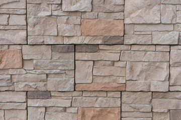 Close-up view of textured beige building wall surface covered with stone shaped tiles. Abstract construction industry background. Copy space. Soft focus. Decor materials theme.