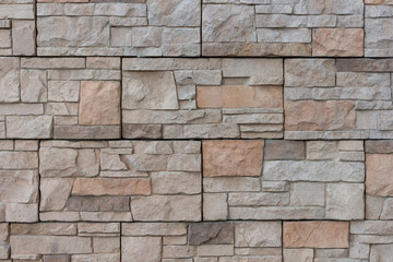 Fototapeta premium Close-up view of textured beige building wall surface covered with stone shaped tiles. Abstract construction industry background. Copy space. Soft focus. Decor materials theme.
