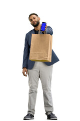 A man, full-length, on a white background, with bags, shows a phone