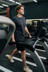 Vertical shot of sporty beginner male walking on treadmill, working on health and fitness in gym....