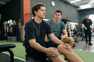 Exhausted sportsman in conversation with personal trainer in gym after workout training on rowing...