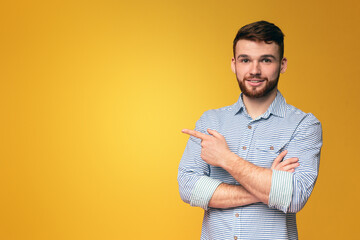 A man with crossed arms standing in front of a bright yellow background, pointing at copy space for advertisement