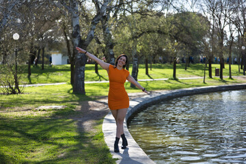 Young, beautiful woman in an orange dress, very happy and content, walking balancing on the curb...
