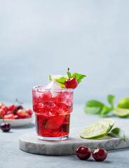 Cherry-lime mojito cocktail with mint, lime and ice on a marble board on a blue background.