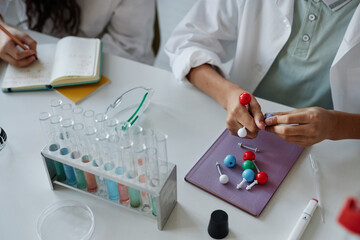 High angle view of unrecognizable kids sitting at desk in classroom assembling chemical structure model and making notes during lesson