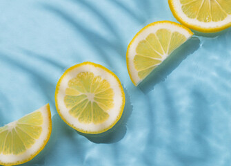 Lemon slices in water on a blue background with shadow and waves close up. Summer refreshing...