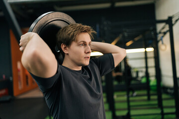 Closeup portrait of dedicated beginner sportsman holding and rotating weight disc plate overhead...