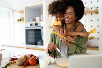 African American mother and daughter laughing and smiling while making pasta and playing with...