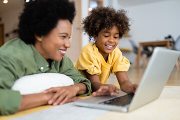 Smiling mother and daughter using laptop while relaxing at home.