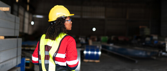 A industrial worker in a yellow helmet and safety vest stands in a warehouse.