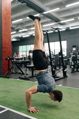 Vertical shot of athletic muscular sportsman doing push ups challenge in handstand at gym. Athlete...