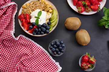 Healthy breakfast. Granola with strawberries, kiwi, banana and blueberries in a round plate on a black table. Healthy and tasty food