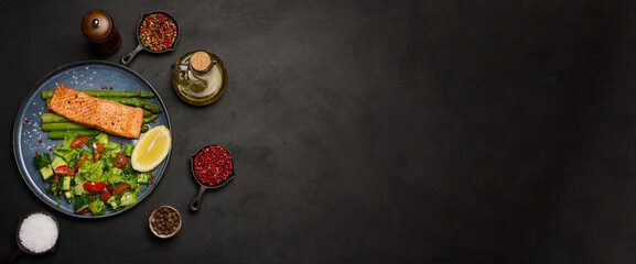 Healthy lunch with grilled salmon with asparagus and fresh tomato and cucumber salad, a row of lemon slice. Food on a blue round plate, top view