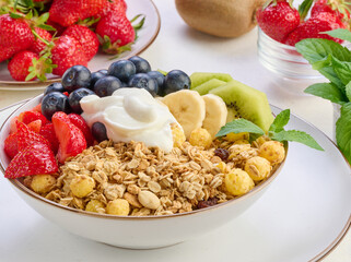 Granola with strawberries, kiwi, banana and blueberries in a round plate topped with yogurt on the table. Healthy and tasty food