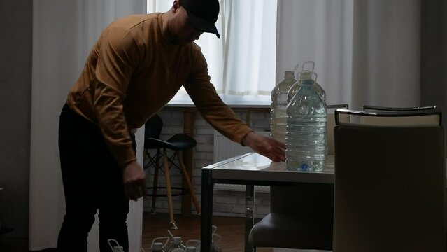  A man puts bottled water on the table. Emergency drinking water in halons. A person stores drinking water in plastic bottles