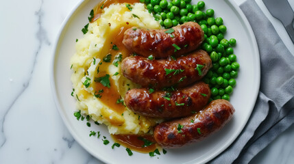 Pork sausages with creamy mashed potatoes, gravy sauce, green peas and greenery on white plate on dark grey background and napkin overhand