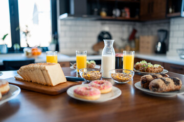 Breakfast food table. Festive brunch set, meal variety with donuts, croissants, sandwiches, milk and orange juice. No people on the photo.