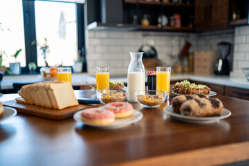 Breakfast food table. Festive brunch set, meal variety with donuts, croissants, sandwiches, milk and orange juice. No people on the photo.