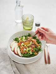 Hand with spoon dressing with vinaigrette a delicious salad of lamb's lettuce, avocado, lentils and apple.