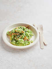 Compostable single-use cardboard plate with healthy food, broccoli and chicken on white table with wooden cutlery.