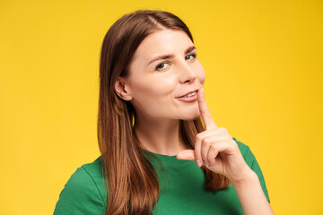 Portrait of excited smiling middle aged woman holding finger near mouth, showing silence sign