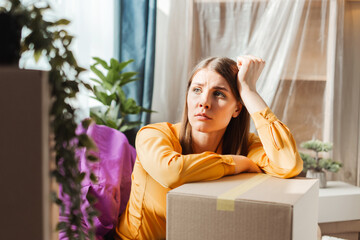 Upset, sad middle aged woman sitting on cardboard boxes looking sadly away, moving, relocation