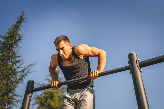 One man muscular male athlete training pull ups outdoor in sunny day