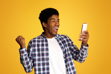 Winner Concept. African Guy Using Smartphone over Yellow Studio Background