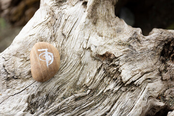 An image of a energy healing symbol painted on a beige rock and set on a natural driftwood log. 