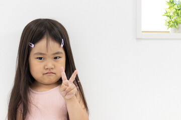 ピースする不満顔の女の子（3歳、日本人）